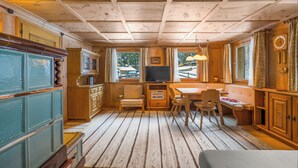 Interior de una cabaña de madera con comedor, cocina y un ventanal grande.