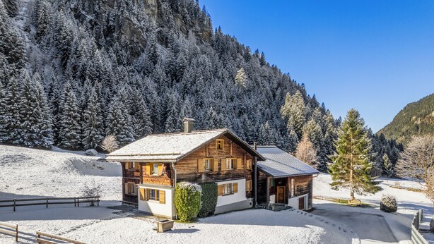 Una cabaña de madera con tejado nevado y una valla de madera al frente.