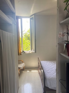Un dormitorio con una cama individual, una ventana con cortinas, un radiador y una planta.