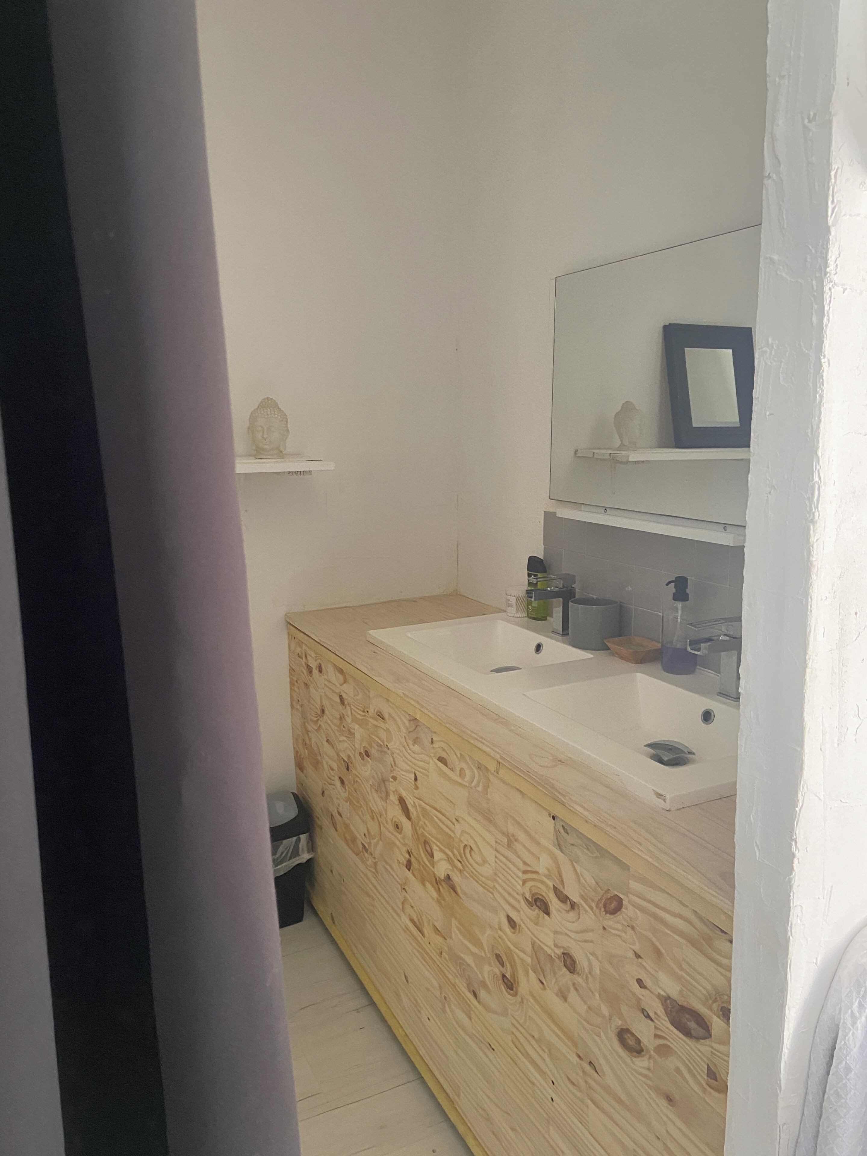 Un baño con tocador de madera, dos lavamanos, un espejo y un pequeño estante con objetos decorativos.