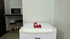 A white refrigerator with the brand name 'Consul' on it, placed in a kitchen area with a microwave and a small table in the background. - Comfort & king bed near Riocentro and Olympic Park (Jacarepaguá Rio de Janeiro)