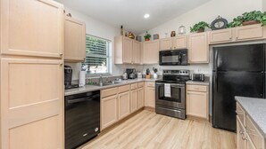 Una cocina moderna con armarios de madera clara, electrodomésticos de acero inoxidable y una ventana con persianas.