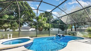 Una piscina con cerramiento de vidrio, un pequeño jacuzzi y un escalón blanco para entrar a la piscina.