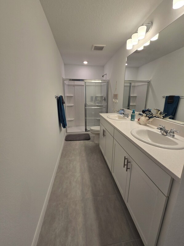 A modern bathroom with a glass shower enclosure, a double sink vanity, and a large mirror. - Beautiful 2-bedroom townhome in Sarasota with WiFi, AC, & two pools. (Sarasota)