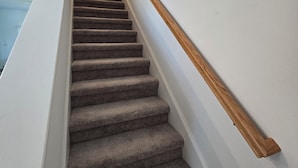 Eine Teppichstufen-Treppe mit einer Holzhandläufe, weißen Wänden und einer Deckenleuchte.