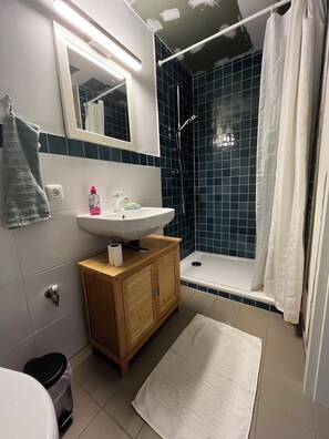 A bathroom with a white sink, wooden cabinet, and a shower with blue tiles. - Beautiful circus wagon in a secluded location  (Oetzen)