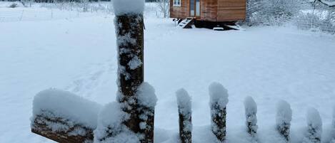 A wooden cabin with a snow-covered roof and a wooden fence in the foreground.
