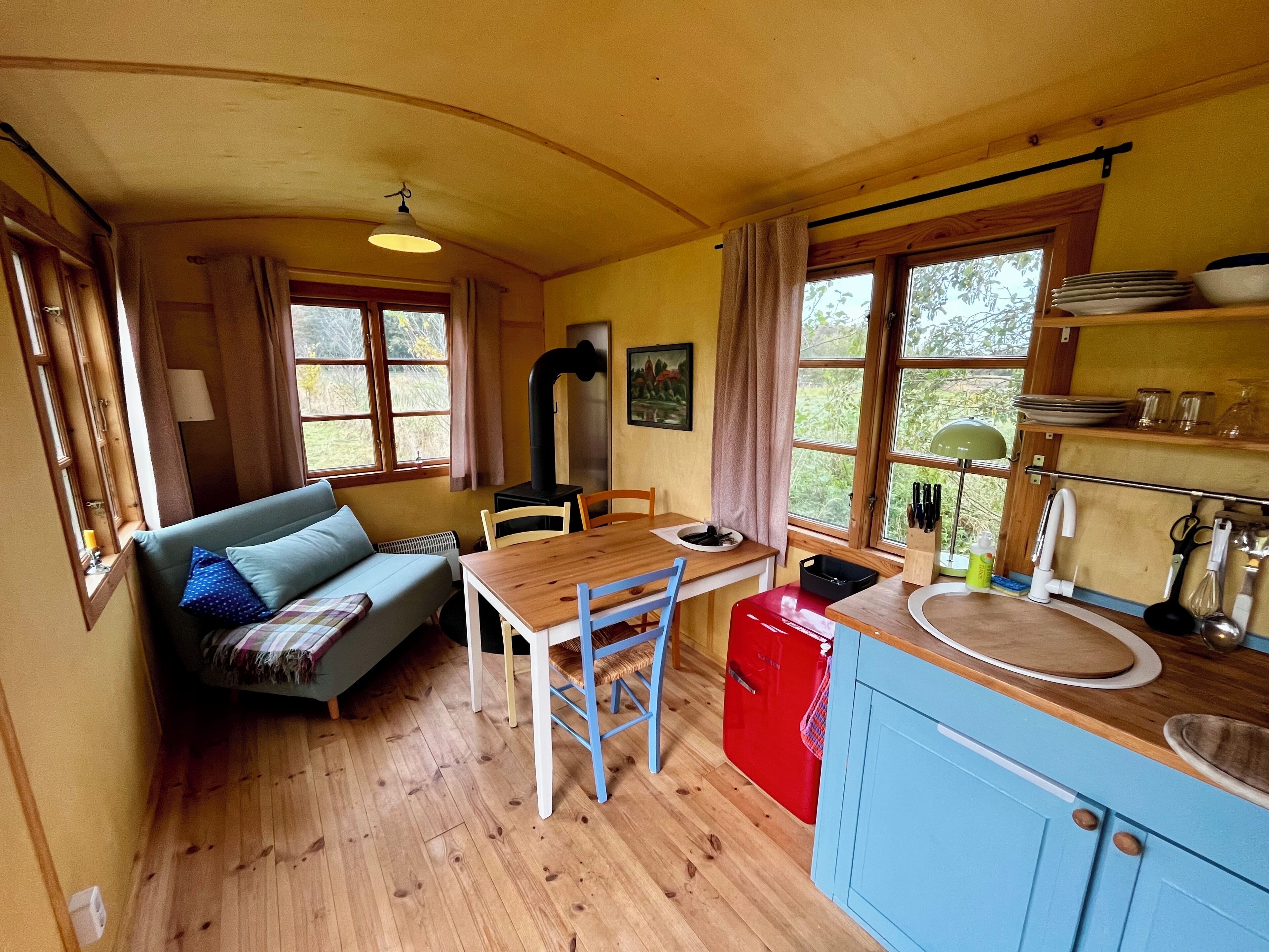 A cozy cabin interior with a wooden dining table, a red kitchen counter, and a blue cabinet.