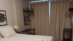 A hotel room with a large bed, a desk, a chair, a lamp, and a view of the outdoors through curtains.