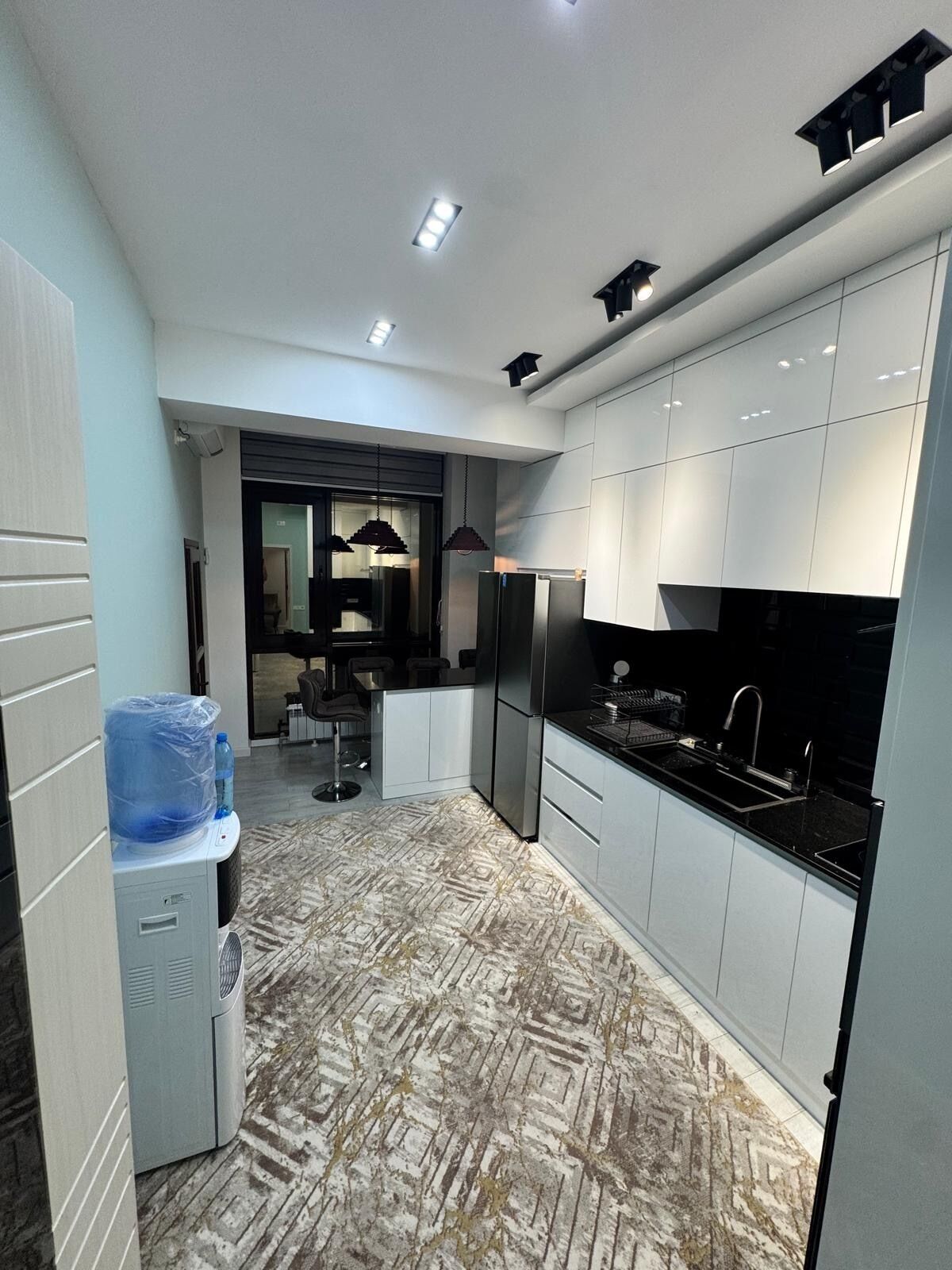 A modern kitchen with white cabinets, stainless steel appliances, and a patterned floor.
