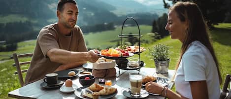 Un couple est assis à une table dressée pour le dîner, en plein air, et est entouré d’un paysage magnifique.