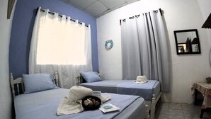 Habitación de hotel con dos camas, cada una con cubrecama y almohadas azules. Hay una toalla sobre la cama y una mesita con mantel.