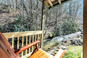 Une terrasse en bois avec un banc donnant sur une zone boisée et un ruisseau.