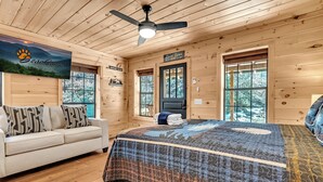 A cozy cabin interior with a wooden ceiling, a bed with a patterned quilt, a sofa with pillows, and a sign reading "Live lines here". - Renovated Barn with Creek and Waterfall (Cosby)