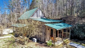 A rustic cabin with a green roof, a porch with chairs, and a stone pathway leading to the entrance. - Renovated Barn with Creek and Waterfall (Cosby)
