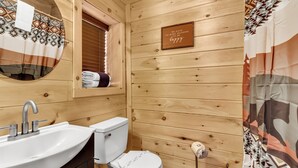 A wooden cabin bathroom with a sink, toilet, and a window with a towel hanging. - Renovated Barn with Creek and Waterfall (Cosby)