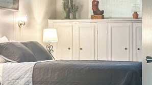 Un dormitorio con cama, ventilador de techo, ventana con persianas, una decoración de cactus y una lámpara.