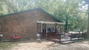 Una cabaña rústica con un porche, una parrilla y un banco rojo.