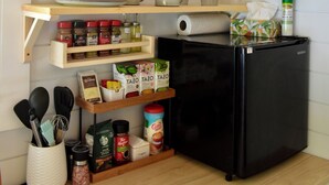 Una cocina con estantes de madera, un refrigerador negro y diversos utensilios de cocina.