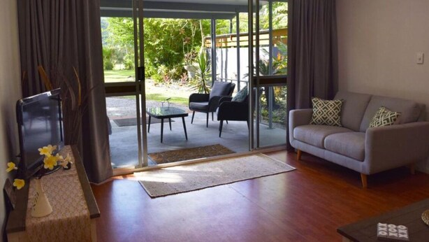 A living room with a sofa, a coffee table, a TV, and a sliding glass door leading to an outdoor patio with chairs and a table.