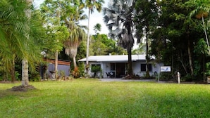 A house with a front porch, surrounded by lush greenery and palm trees.