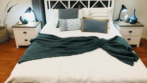 A neatly made bed with a green blanket, white bedding, and patterned pillows. There are two bedside tables with lamps and decorative items.