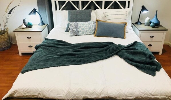 A neatly made bed with a green blanket, white bedding, and patterned pillows. There are two bedside tables with lamps and decorative items. - Egrets Rest Daintree (Daintree)