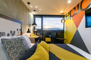 Une chambre d’hôtel moderne, équipée d’un lit, d’un bureau et offrant une vue sur les montagnes.