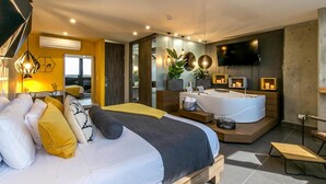 Une chambre d’hôtel moderne dotée d’un grand lit, d’un coin salon avec un canapé, d’un téléviseur fixé au mur et d’une petite table.