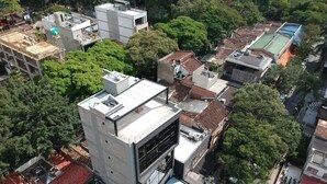 An aerial view of a residential area with a modern two-story building, surrounded by trees and traditional houses.