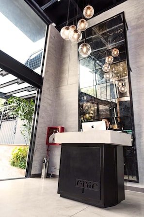 A modern interior with a large glass wall reflecting the outside, a minimalist black counter, and hanging spherical light fixtures. - Epic Boutique Hotel (Medellín)