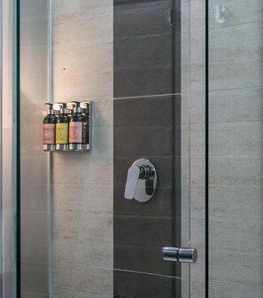Un espace douche doté d’une porte en verre, d’un robinet métallique et d’une bouteille de shampoing posée sur une étagère.
