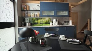 Een moderne keuken met blauwe kastjes, een ronde eettafel en uitzicht op een bos.