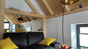 Een moderne woonkamer met een zwarte leren bank, gele kussens, een glazen salontafel en een bloevas.