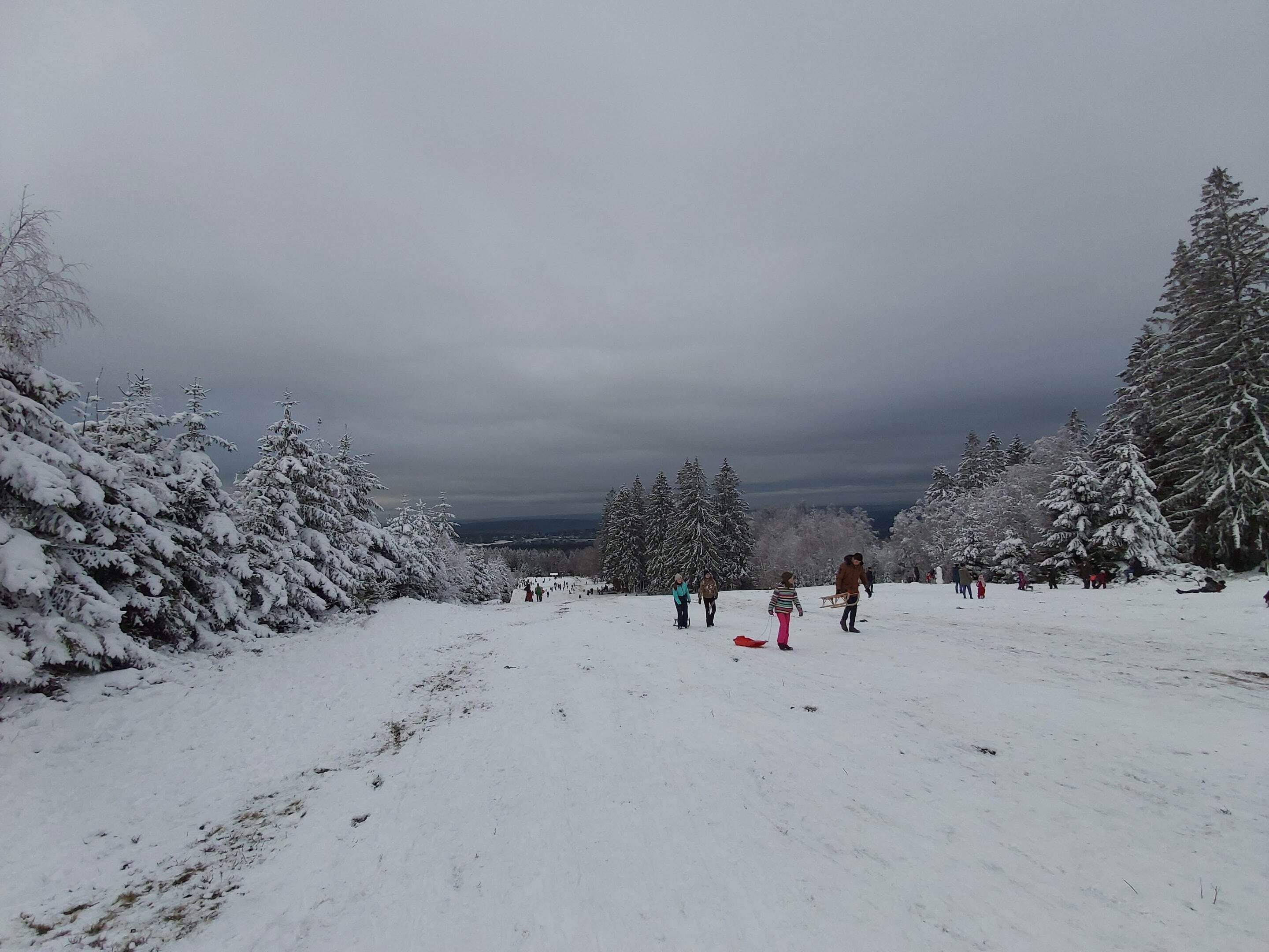 Un paysage enneigé où l’on voit des personnes se promener et faire de la luge.
