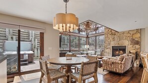 A spacious living room with a stone fireplace, a round dining table with chairs, and a large window overlooking a deck. - Stonebridge  (Park City)