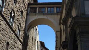 Une rue étroite bordée d’immeubles en pierre, un pont en arc et un ciel d’un bleu limpide.