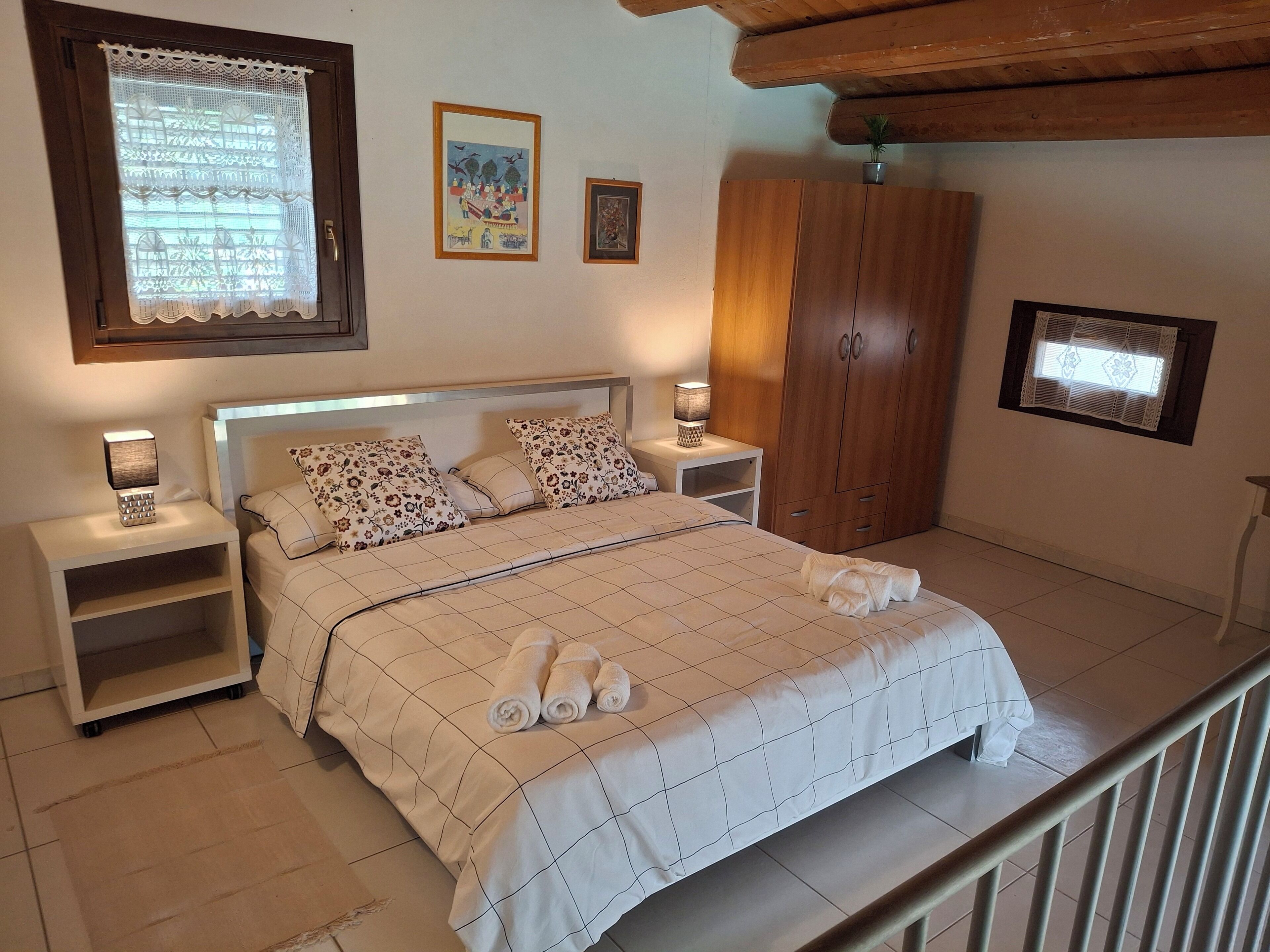 Une chambre à coucher avec un lit, des tables de chevet, une armoire et une fenêtre ornée de rideaux en dentelle.