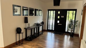 A hallway with a wooden floor, a console table with decorative items, a black door with windows, and a potted plant.