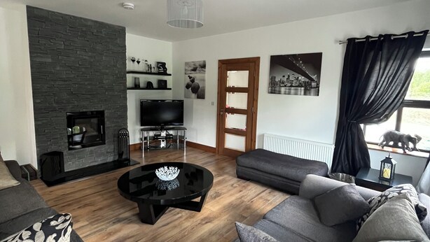 Un salon moderne avec une cheminée en pierre, des canapés gris, une table basse noire et un plancher en bois.