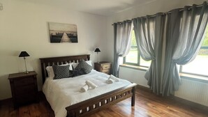 Une chambre à coucher avec un lit en bois, deux tables de chevet, un luminaire au plafond, une fenêtre avec des rideaux et un tableau accroché au mur.