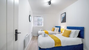 A hotel room with two beds, a window, a painting, and a bedside table with a lamp. - Deluxe 3 Bedstratford Apartment Olympicparko2excel (London)