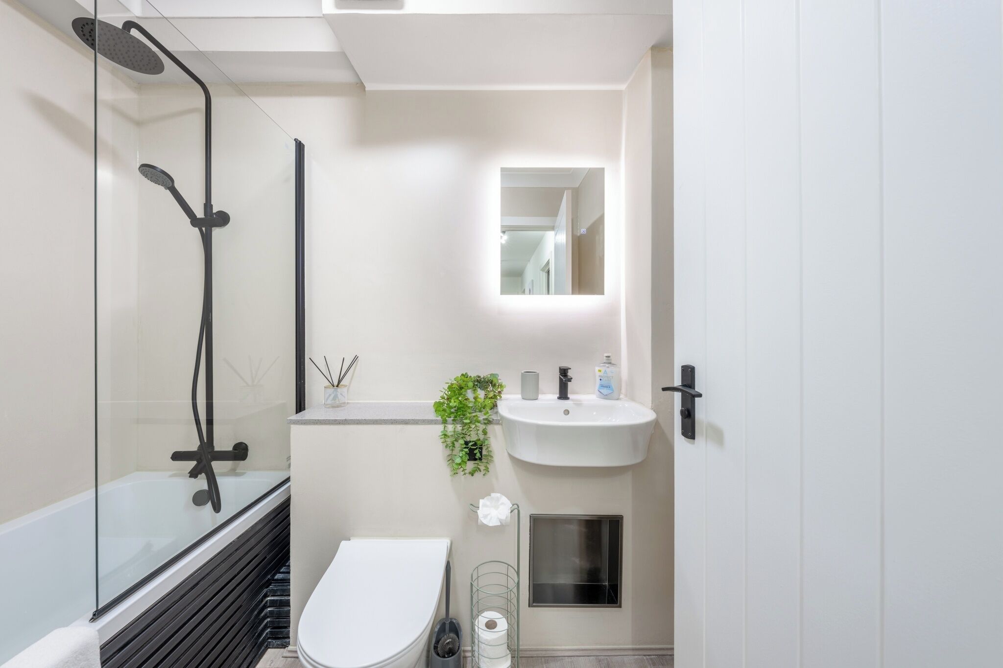 Une salle de bain moderne avec une douche à parois de verre, des toilettes blanches et un lavabo avec un miroir au-dessus.