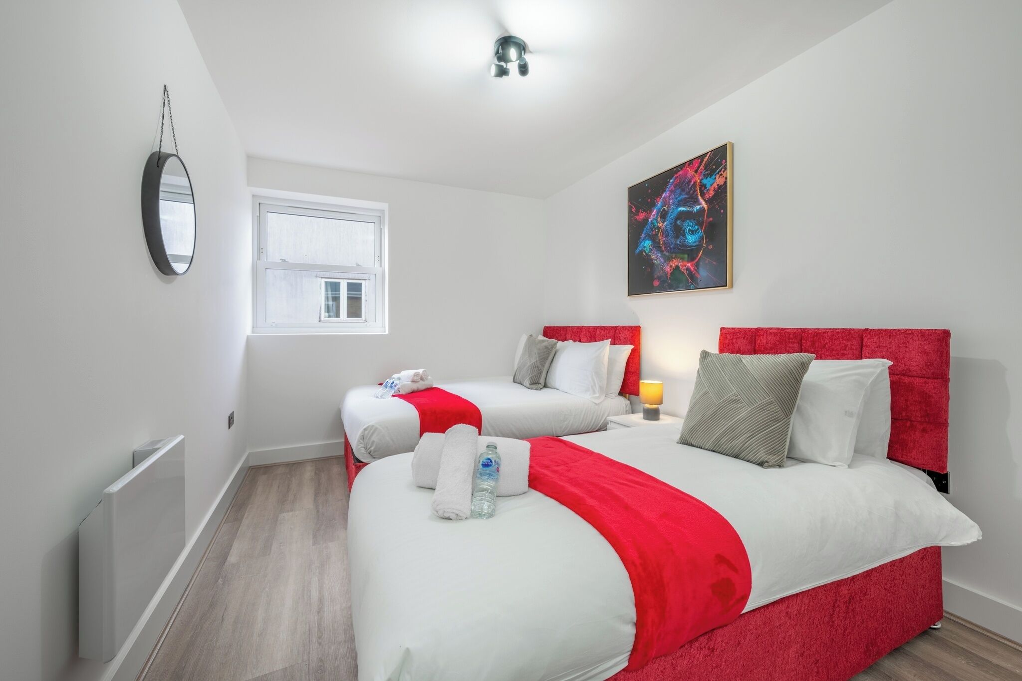 A hotel room with two beds, a large window, a ceiling fan, and a painting on the wall.