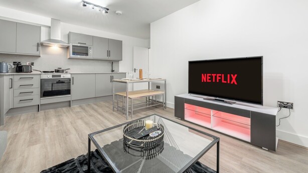A modern kitchen with built-in appliances, a dining area with a bench, and a TV displaying the Netflix logo. - Deluxe 3 Bedstratford Apartment Olympicparko2excel (London)