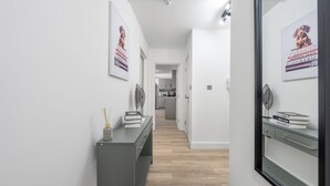 A modern hallway with a grey console table, a mirror, and framed posters on the walls. - Deluxe 3 Bedstratford Apartment Olympicparko2excel (London)