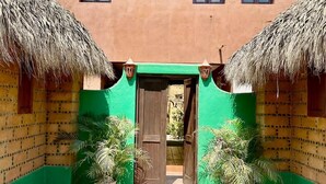 A building with a green facade, a central wooden door, and two thatched-roof structures on either side. - Charming 2-bedroom apartment  in COL Majahua, Troncones, Mexico GRO. (COL Majahua)