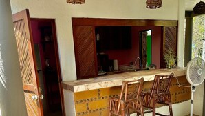 A kitchen area with a bar counter, stools, hanging wicker light fixtures, and a fan. - Charming 2-bedroom apartment  in COL Majahua, Troncones, Mexico GRO. (COL Majahua)