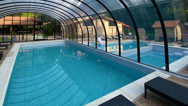 An indoor swimming pool with a glass ceiling, surrounded by lounge chairs and a stone wall in the background. - Aufenthalt Cabañas (Villa General Belgrano)