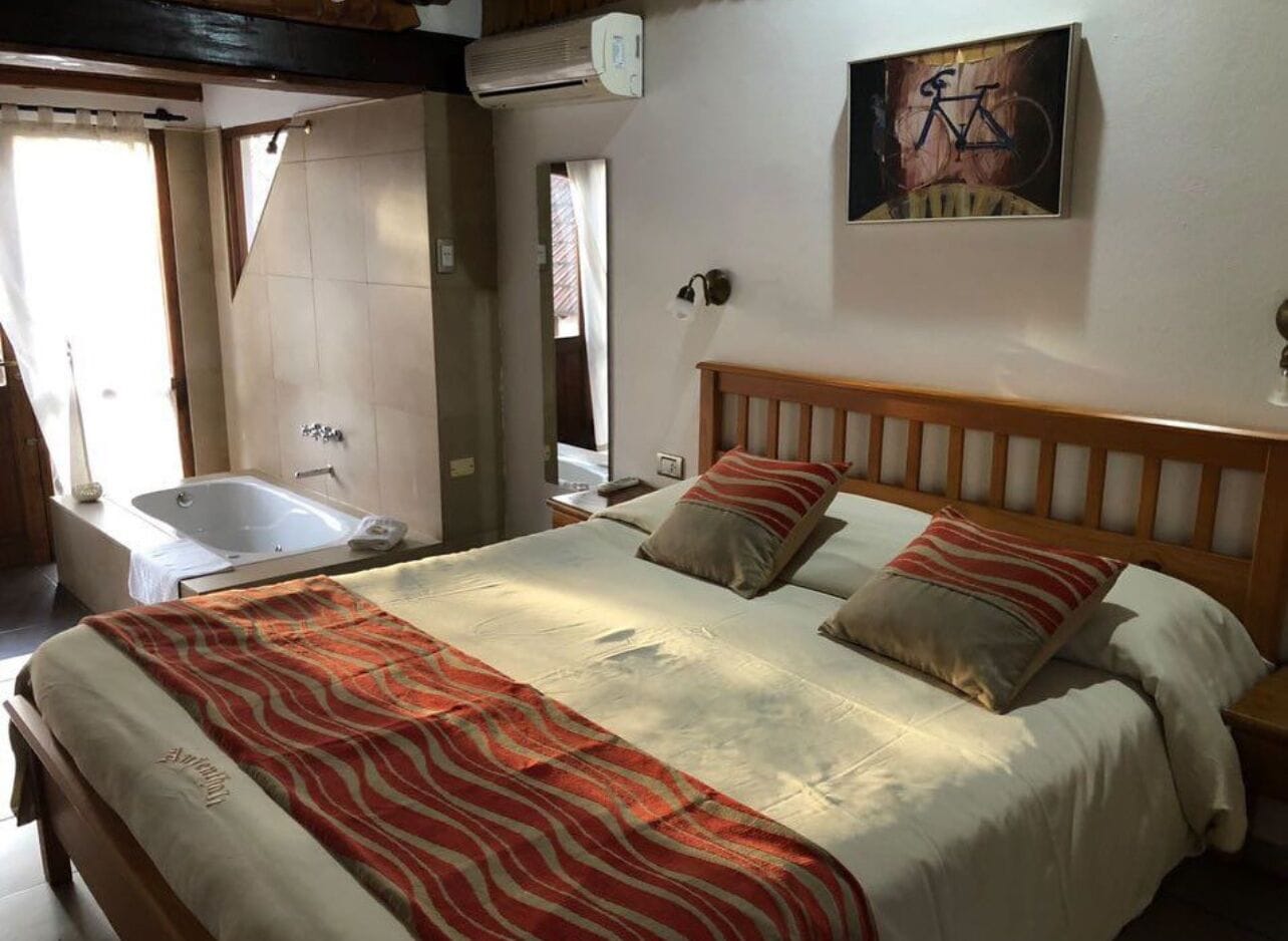Ein Schlafzimmer mit einem großen Bett, einem hölzernen Kopfteil, einem Bild von einem Fahrrad, einem Fenster und einem Badezimmer mit einer Badewanne.